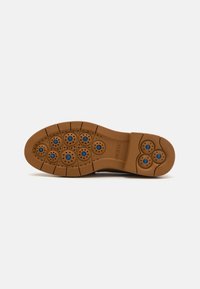 Suela de zapato de goma color bronce con agarres texturizados en forma de círculos, que presenta acentos en azul y orificios de ventilación. Acabado suave con diseño segmentado.