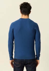 Blauwe geribbelde trui met lange mouwen, ronde halslijn en accentuerende taille. Bevat een gestructureerde stof en een subtiele zijnaadaccent.