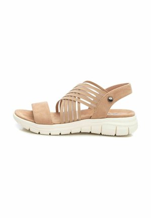 Sandalia beige con múltiples correas elásticas, una plantilla de ante suave y una suela de goma blanca y ligera, con un acento plateado en el lateral.