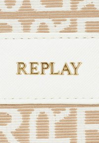 Etichetta in tessuto beige e bianco con una texture, che presenta la parola "REPLAY" in lettere dorate. L'etichetta ha un bordo cucito e un motivo sottile.
