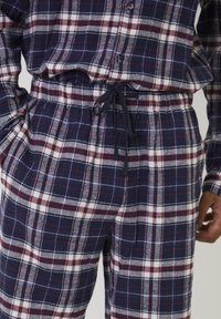 Conjunto de pijama de cuadros en azul marino, blanco y rojo con cintura elástica y cordón ajustable, mangas largas y parte delantera de camisa abotonada.