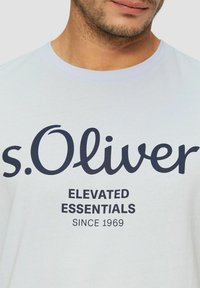 Light blue cotton t-shirt featuring a dark blue print with the brand name "s.Oliver," and the text "ELEVATED ESSENTIALS SINCE 1969."