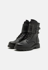 Botas de tobillo de cuero negro con diseño de cordones, detalles texturizados y dos hebillas laterales adornadas con tachuelas plateadas. Suela de goma gruesa.