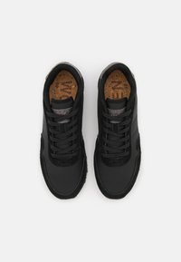 Black athletic shoes with a suede and synthetic upper. Features laces, a textured grey accent at the heel, and a cork insole.