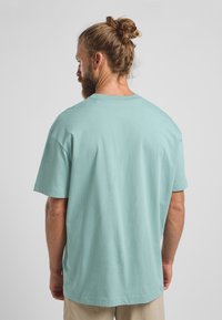 Mintgrünes Baumwoll-T-Shirt mit entspannter Passform, kurzen Ärmeln und rundem Halsausschnitt, mit einem Etikett an der Seitennaht.
