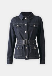 Mørk denimjakke med lange ermer, knappelukking, to frontlommer og beltestropp i livet. Har sølvfargede knapper og kontraststing.