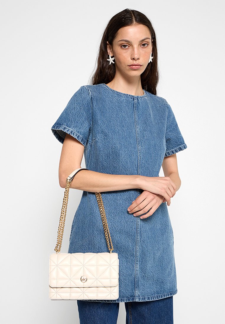 Jeanskleid mit kurzen Ärmeln und rundem Ausschnitt. Beigefarbene gesteppte Handtasche mit goldener Kettenriemen. Modell trägt Ohrringe und steht vor einem schlichten Hintergrund.