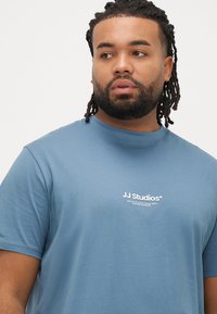 Kortærmet blå bomuld T-shirt med rund halsudskæring og hvidt trykt logo på brystet, med en glat og jævn tekstur.