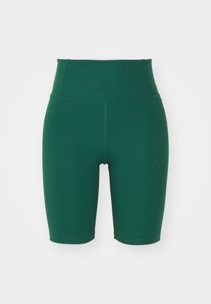 Shorts de vélo verts à côtes avec une taille haute, présentant une texture lisse et un ajustement serré. La longueur atteint le milieu de la cuisse.