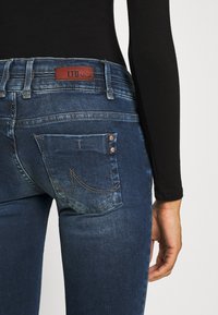 Jeans de mezclilla de un azul oscuro que presentan una etiqueta de cuero LTB, bolsillos traseros con detalles de costura y un ligero desgastado para una apariencia texturizada.