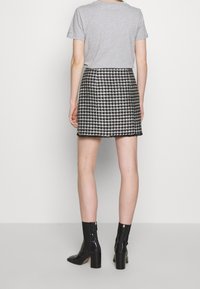 Šedé tričko spojené s černo-bílou minisukní v kašmírovém vzoru, doplněné černými lakovanými kotníkovými botami s blokovým podpatkem.