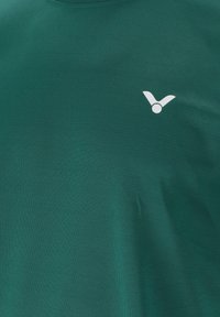 Mörkgrön kortärmad t-shirt gjord av slätt tyg. Har en liten vit logga på vänster bröstområde. Rund halsringning.