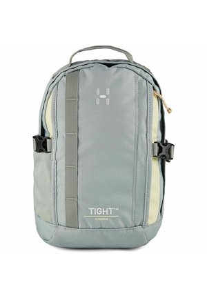 Mochila compacta en gris y beige con asa superior, hebillas laterales, correa vertical frontal y la marca "TIGHT Junior 8" en el panel frontal.