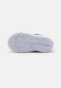 Weiße Sneaker-Sohle mit strukturiertem Grippattern, versehen mit einem markanten Nike-Logo und geformten Traktionselementen. Das Obermaterial hat blaue Akzente.
