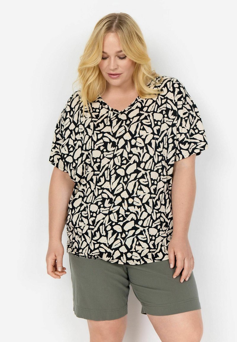 Korte mouwen V-hals top met een zwart en beige abstract patroon op een lichte stof, gecombineerd met olijfgroene shorts.
