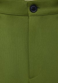 Olijfgroene broek van gladde stof; heeft een voorzak, een enkele zwarte knoopsluiting en scherp afgewerkte stiksels.