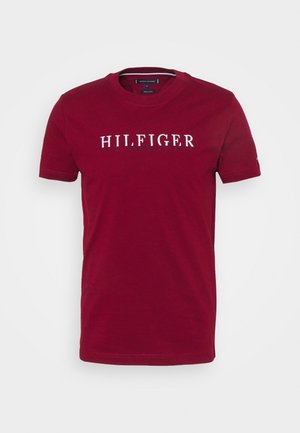 T-shirt rouge à manches courtes avec col rond et texte blanc "HILFIGER" sur la poitrine sur un fond blanc uni.