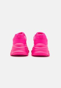 Zapatilla de deporte de color rosa brillante con una superficie lisa y texturizada. Presenta un tacón acolchado y un diseño de suela redondeada para mayor comodidad y soporte.