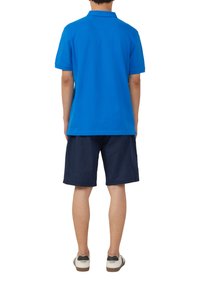 Blauwe poloshirt met een klassieke kraag, gecombineerd met marineblauwe shorts. De outfit wordt compleet gemaakt met witte sneakers met donkere accenten.