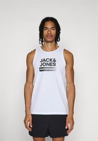 Camiseta sin mangas blanca con el texto negro "JACK & JONES PERFORMANCE"; material de algodón suave, corte relajado, diseño sencillo, cuello redondo.