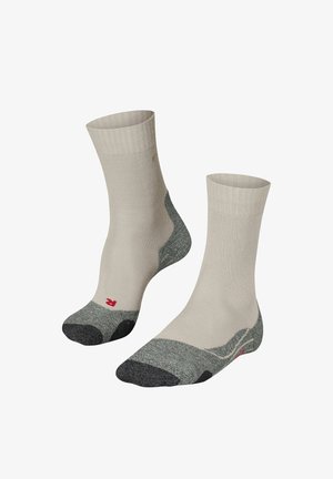 Beige sokken met een geribbelde textuur, voorzien van een grijze teen- en hielsectie en een rood logo aan de onderkant. Halflange lengte tot de kuit.