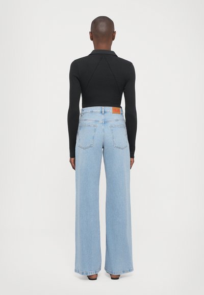 Wide-leg light blue jeans with a high waist, finished hem, and rear pockets; paired with a fitted black long-sleeve top featuring a collar.