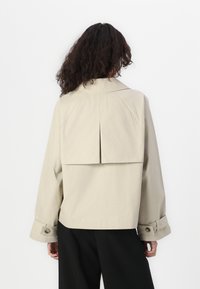 Beige oversized jacket with a back pleat, structured collar, and cuffs featuring button accents. Made of smooth, lightweight fabric.