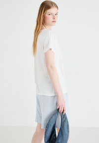 Haut blanc à manches courtes en tissu léger, associé à un short bleu clair ; tenant une veste en denim. Design simple et épuré.