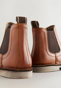 Stivaletti Chelsea in pelle marrone con pannelli laterali elastici, suola piatta in gomma e linguette per una facile vestibilità. I dettagli cuciti conferiscono struttura.