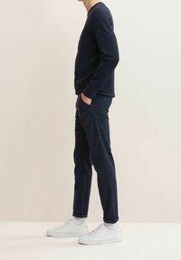 Námořnická mikina s dlouhými rukávy v kombinaci s úzce střiženými tmavě kostkovanými kalhotami a bílými teniskami. Tento outfit má neformální, přiléhavý siluetu.