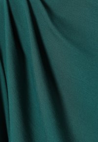 Tkanina v barvi modrozelene, ogrnjena tako, da prikazuje teksturo, z gladko površino in rahlim sijajem, ki vsebuje tkan vzorec in mehak videz.