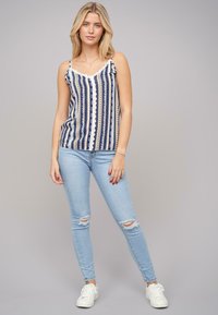 Tumesinine ja kreemika mustriga tank top pitsäärisega, millele on sobitatud helesinised rebenditega kitsad teksad ja valged spordijalatsid. Igapäevane outfit, põlvini ulatuv disain.