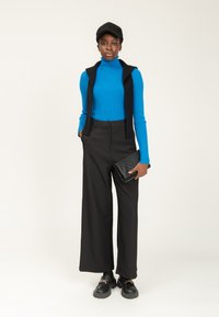 Maglione a collo alto blu a coste, gilet nero corto, pantaloni larghi neri, pochette nera testurizzata e scarpe nere chunky.