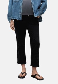 Pantaloni cropped neri con una texture liscia, vita aderente e un leggero svaso all'orlo, abbinati a una giacca di jeans blu e infradito.
