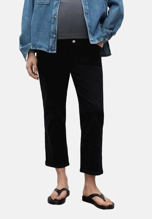 Black cropped pants with a smooth texture, a fitted waist, and slight flare at the hem, paired with a blue denim jacket and flip-flops.