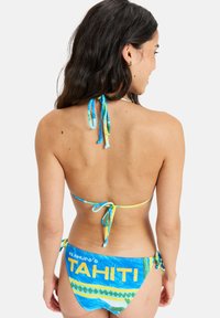 Bikini med ett färgglatt tropiskt mönster i blått, grönt och gult. Har knytband och ordet "TAHITI" tydligt synligt på baksidan.