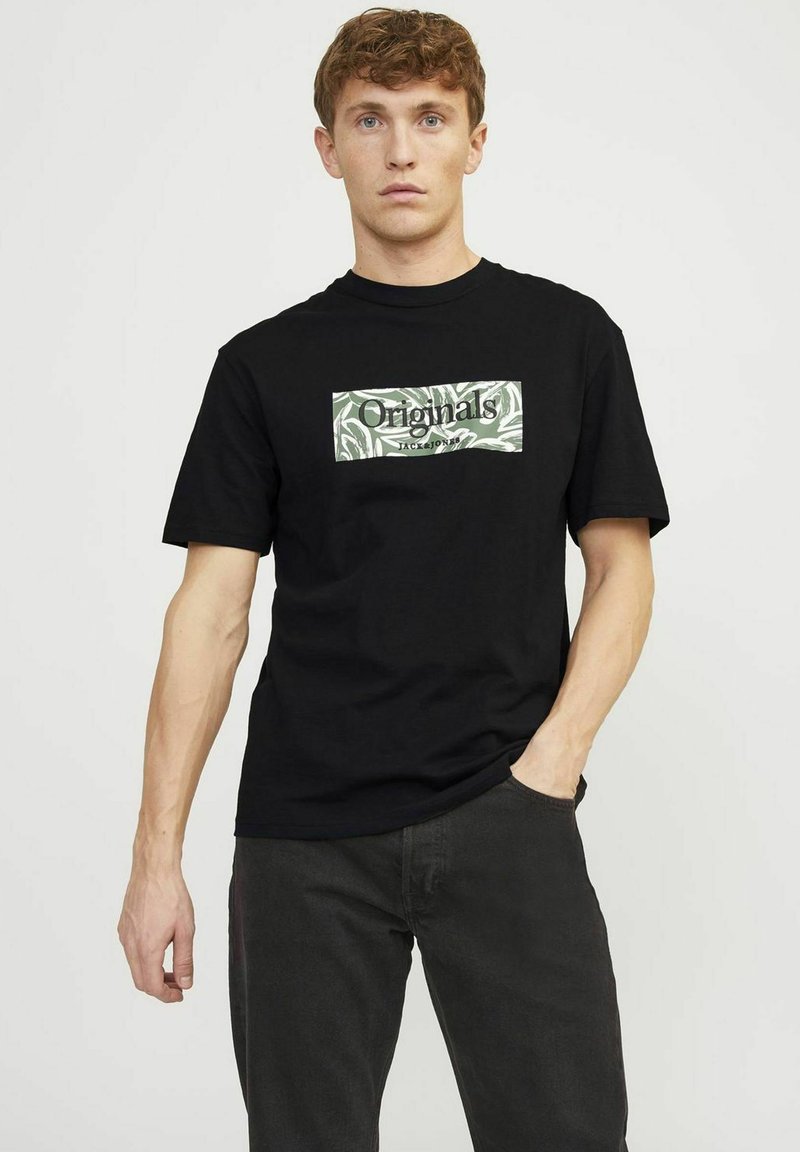 Schwarzes Baumwoll-T-Shirt mit einem rechteckigen grünen und weißen Grafik, auf der das Wort "Originals" in einer fetten Schriftart abgebildet ist. Mit kurzen Ärmeln und Rundhalsausschnitt.