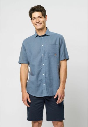 Kurzarmhemd mit Kragen aus hellblauem Stoff mit strukturiertem Finish, ausgestattet mit einer Brusttasche und kleinem Emblem. Kombiniert mit navyblauen Shorts.
