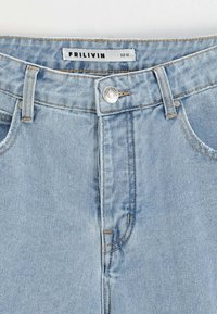 Jean en denim bleu clair à taille haute, avec des coutures orange, une fermeture à bouton argenté et des poches avant. Étiquette de taille visible sur la taille.