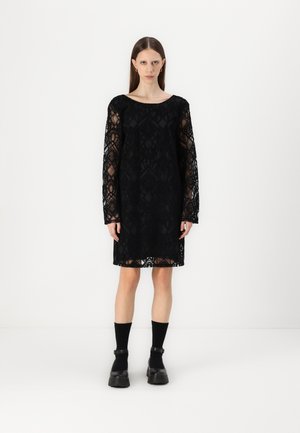 Black lace dress with long sheer sleeves, square neckline, and floral patterns. Finished with a scalloped hem, paired with chunky black footwear.