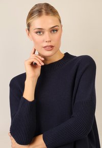 Granatowy sweter dziergany z okrągłym dekoltem i prążkowanymi akcentami na rękawach, charakteryzujący się miękką teksturą i luźnym krojem.