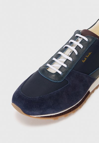 Navy suede and leather sneaker with white laces, navy canvas sections, and a brown accent. Features a textured sole for grip.