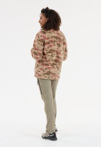 Fleecejacka i rosa, grön och beige kamouflagemönster med långa ärmar. Tillsammans med kaki cargobyxor och lätta vandringsskor.