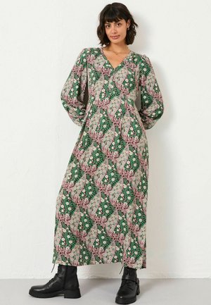 Long, patterned dress with a deep V-neck, balloon sleeves, and a floral design in green, pink, and beige. Paired with black ankle boots.