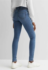 Siniset slim-fit-farkut, joissa on keskitason vyötärö, klassinen viiden taskun malli ja ompelukoristeet. Yhdistetty valkoisiin lenkkareihin.