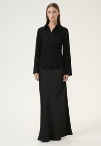 Black textured long-sleeve shirt with a collared neckline and button front, paired with a black smooth floor-length skirt.