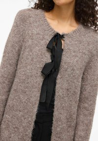 Biezi brūni džemperis ar mīkstu faktūru, ar apaļu kakla izgriezumu un atslēgas caurumu, ko droši tur ar melnu lentu.