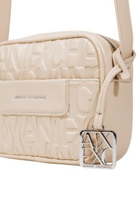 Borsa a tracolla in finta pelle crema con logo impresso, chiusura con zip e un ciondolo in metallo argentato con le iniziali del marchio.