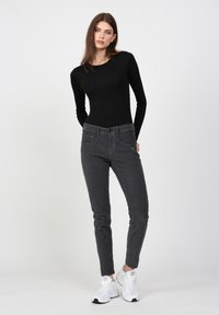 Schwarzes Langarmoberteil kombiniert mit grauen Slim-Fit-Hosen mit vorderen Taschen. Das Model trägt weiße Sneakers. Schlichter Hintergrund, keine zusätzlichen Details.