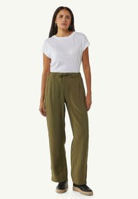 Olivengrüne, locker sitzende Hose mit elastischem Bund und Kordelzugdetails. Kombiniert mit einem schlichten weißen T-Shirt und schwarzen Sneakers.